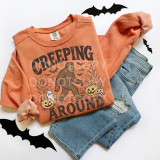 Creeping Around DTF Heat Transfer, Halloween-themed t-shirt with a cartoon Bigfoot, pumpkins, and bats on an orange sweatshirt, paired with distressed denim shorts.