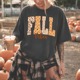 Patterned Fall Vibes DTF Heat Transfer on a black T-shirt with autumn-themed designs, worn by a woman with tattoos holding iced coffee at a pumpkin patch.