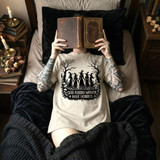 God Forbid Women Have Hobbies Halloween DTF Heat Transfer, woman lying in bed with a book covering her face, wearing a Halloween-themed T-shirt with witch silhouettes and trees.