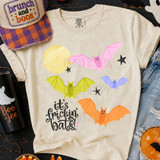 It's Frickin' Bats Colorful Halloween DTF Heat Transfer, playful design featuring pink, yellow, purple, and orange bats flying across a cream-colored T-shirt with moon and star accents.