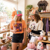 Shop Small Puff Embroidered Hat Patch, two women wearing colorful hats with embroidered patches shopping in a boutique with halloween-themed decorations and trendy clothes.
