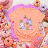 Pastel Pumpkin Patch DTF Transfer, boho fall floral pumpkins design printed on peach and lavender T-shirts surrounded by fall-themed decor including mini pumpkin decorations, knitted scarves, and vibrant flowers for autumn fashion.