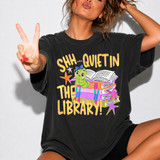Shh… Quiet in the Library DTF Transfer | Cute Librarian Bookworm Heat Transfer, a woman showing off a colorful and playful heat transfer design on a black t-shirt featuring a cartoon caterpillar, books, and stars with text 'Shh... Quiet in the Library!'