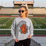 Dotted Mascot DTF Transfers | School Spirit Mascot Collection, a sweatshirt featuring a cartoon tiger mascot with stars around it, worn by a woman standing on a football field.