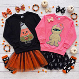 Candy Corn Witch Youth Sequin Patch, two children's sweaters with Halloween-themed sequin patches of a candy corn witch and a mummy, paired with Halloween accessories like ghost and pumpkin socks, bows, and pumpkin decorations.