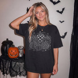 Patterned Pumpkins DTF Transfer | White Checker Plaid Floral Pumpkin Heat Transfer, Halloween themed image showing a woman wearing a black T-shirt with white pumpkin designs, surrounded by Halloween decorations.