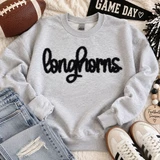 Black Longhorns fluffy heat press appliqué patch with script lettering displayed on a light gray sweatshirt.