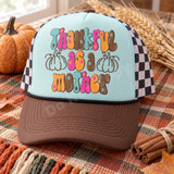 Thankful As A Mother DTF transfer in retro bubble lettering with brown line-art pumpkins on a beige shirt Shown on a Chalky Mint front panel, brown bill, black-and-white checkered mesh back trucker hat.