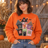 Whimsical patchwork haunted house DTF transfer with gingham, leopard, floral, and polka dot fabric-style panels, blanket-stitch edges, bats, and a purple crescent moon Shown on a Orange crewneck sweatshirt.