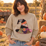 Patchwork witch hat DTF transfer with plaid, gingham, floral, and leopard fabric patches joined by orange whip-stitching and a plaid buckle Shown on a Sand crewneck sweatshirt.