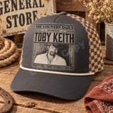 Toby Keith DTF transfer designed as a vintage newspaper front page with distressed photo and 'Should've Been a Cowboy - As Good As I Once Was' headline Shown on a charcoal front panel with cream rope and brown-and-tan checkered mesh back trucker hat.