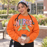 NURSE DTF transfer in patterned bubble letters with green zombie hands and pink claw nails forming a heart Shown on a Orange crewneck sweatshirt.