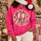 Pink smiley face DTF transfer filled with hand-painted pink, green, teal, and cream Christmas trees and decorative bows Shown on a Heliconia crewneck sweatshirt.
