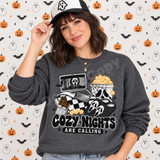Cozy Nights Are Calling Halloween DTF transfer with laptop playing horror movie, checkered blanket, chocolate bar, skull popcorn bucket, and ghost-face slippers Shown on a Graphite Heather crewneck sweatshirt.