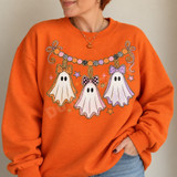Pastel ghost garland DTF transfer with three bow-topped ghosts in orange, pink, and purple strung beneath a beaded candy-colored banner with stars and glitter accents Shown on a Orange crewneck sweatshirt.