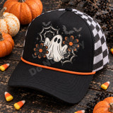 Spooky-cute ghost DTF transfer with glitter-style stitching, black lace spiderwebs, bats, stars, and orange daisy flowers in a Halloween patch design Shown on a Black front panel and bill with an orange rope accent, black-and-white checkered mesh back trucker hat.