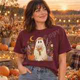Whimsical floral ghost DTF transfer holding a wildflower bouquet with pumpkins, autumn flowers, and a crescent moon Shown on a Wine t-shirt.