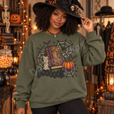 Boooook Halloween DTF transfer featuring a stitched spellbook with glowing eye, snake, bats, spiderwebs, candle, and jeweled pumpkin Shown on a Military Green crewneck sweatshirt.