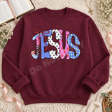 JESUS DTF transfer in colorful bubble letters with polka dot, star, and circle patterns and a red ribbon bow on the J Shown on a Maroon crewneck sweatshirt.