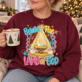 Behold The Lamb of God nativity DTF transfer with baby Jesus in a manger, Star of Bethlehem, lambs, and scalloped pink striped border Shown on a Maroon crewneck sweatshirt.