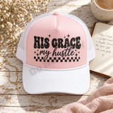 His Grace My Hustle retro bubble letter and cursive script DTF transfer with stars and checkerboard band in worn vintage black texture Shown on a blush pink front panel, white bill, white mesh back trucker hat.