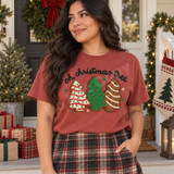 Oh Christmas Tree DTF transfer with three crocheted-look Christmas tree cookie designs in red and white, green, and gingerbread icing styles, surrounded by stars, under black brush-script lettering Shown on a Brick t-shirt.
