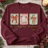 The Lord Is My Shepherd Christmas DTF transfer with scalloped candy-cane striped panels featuring a red bow, fluffy lamb, and ribboned cross above Psalm 23:1 hand-lettered scripture Shown on a Heather Dark Maroon crewneck sweatshirt.