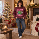 Hot Cocoa Season DTF transfer with a Christmas tree shaped mug filled with cocoa and marshmallows, string lights, ornaments, a red bow, and snowflakes Shown on a Heather Dark Maroon crewneck sweatshirt.