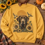 Chocolate Labrador retriever DTF transfer with blooming sunflowers, flying doves, and a glowing orange sunrise Shown on a Gold crewneck sweatshirt.