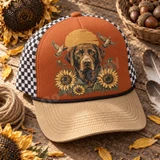 Chocolate Labrador retriever DTF transfer with blooming sunflowers, flying doves, and a glowing orange sunrise Shown on a burnt orange front panel with tan corduroy bill and black-and-white check mesh back trucker hat.