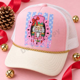 Holly Jolly nutcracker face DTF transfer with pink and gold design, red bow, green crown, and fluffy white beard in a pink scalloped medallion over a blue polka-dot striped background Shown on a blush pink front panel, ivory bill, white mesh trucker hat.