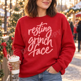 Resting Grinch Face DTF transfer in soft pink hand-lettered cursive script on a green shirt, funny Christmas holiday design Shown on a Cardinal Red crewneck sweatshirt.