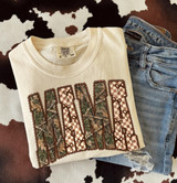 Camo Mama DTF Transfer | Checkered & Bow Lettering Design, cream T-shirt featuring tall “MAMA” letters with camouflage and brown checkered patterns, decorative bows, and scalloped outlines, styled with denim jeans on a cow-print background.