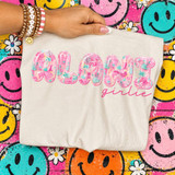 Alani Girlie DTF transfer with collage-style pink and teal Alani Nu print letters and pink script lettering on a cream shirt