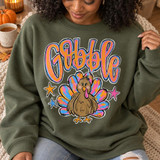 Gobble Turkey DTF Transfer | Retro Tie-Dye Thanksgiving Design, colorful retro “Gobble” lettering and a cartoon turkey with tie-dye feathers printed on an olive green sweatshirt, modeled in a cozy autumn setting.