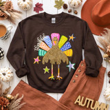 Thankful Turkey DTF Transfer | Colorful Fall Thanksgiving Design, colorful turkey with patterned feathers, stars, and “thankful” lettering displayed on a brown sweatshirt in an autumn-themed flat lay