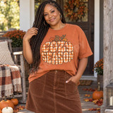 Cozy Season DTF Transfer | Gingham Plaid Fall Bubble Letter Design, orange fall T-shirt featuring large “Cozy Season” bubble lettering in orange-and-cream gingham plaid with autumn leaves and a pumpkin, modeled outdoors in a festive fall setting.