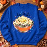 Here For The Mashed Potatoes DTF Transfer | Funny Thanksgiving Food Design, colorful mashed potato bowl with butter and the phrase “Here for the mashed potatoes” displayed on a royal blue sweatshirt surrounded by autumn leaves and pumpkins.
