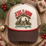 Jesus Is Born Hallelujah DTF Transfer | Vintage Nativity Christmas Design, vintage nativity scene with “Jesus Is Born” and “Hallelujah” lettering displayed on a cream and brown trucker hat among festive Christmas greenery and ornaments.