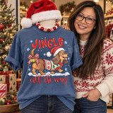 Jingle All The Way DTF transfer with a dachshund in a Santa hat and Christmas sweater, candy-cane bow and bells on its tail, trotting through snow Shown on a Mystic Blue t-shirt.