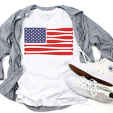 Baseball Flag Sublimation Transfer, white T-shirt with a patriotic American flag design featuring stars and stripes, displayed with a gray shirt, white sneakers, and casual accessories.