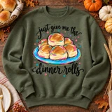 Just Give Me The Dinner Rolls DTF Transfer | Funny Thanksgiving Food Design, colorful illustration of golden dinner rolls on a plate with playful lettering printed on an olive green sweatshirt, styled with autumn leaves and pumpkins.
