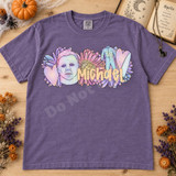 Pastel Michael Myers mask DTF transfer with retro daisies, hearts, coveralls, and butcher knife, lettered with the name Michael in peachy script Shown on a Violet t-shirt.