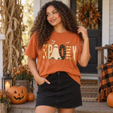 Spooky folk-art DTF transfer with patterned patchwork letters, a ghost replacing the O, a jack-o-lantern by the K, and flying bats above Shown on a Burnt Orange t-shirt.