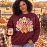 Boutique Turkey DTF Transfer | Psalm 136:1 Thanksgiving Bible Verse Design, colorful patchwork turkey with Psalm 136:1 Thanksgiving Bible verse printed on a maroon sweatshirt, modeled outdoors in an autumn pumpkin patch