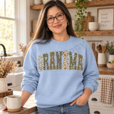 Grandma Patchwork Varsity DTF Transfer | Camo, Leopard & Floral Letter Design, patchwork varsity-style “GRANDMA” lettering in camouflage, leopard print, floral and checkerboard patterns displayed on a light blue sweatshirt