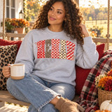 MEMAW Varsity Patchwork DTF Transfer | Boutique Grandma Gift Design, red and cream varsity-style “MEMAW” lettering with assorted patchwork patterns displayed on a gray sweatshirt worn by a woman sitting on a porch swing.
