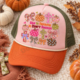 God Is Faithful In Every Season DTF transfer with polka-dot and floral pumpkins, plaid bows, and floral crosses in a colorful hand-lettered fall faith design Shown on a blush pink front panel, burnt orange bill, olive mesh back with cream rope trucker hat.