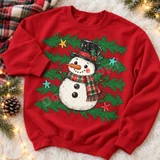 Rustic hand-drawn snowman DTF transfer with black top hat, holly berries, red-and-green plaid scarf, pine branches, and colorful outlined stars Shown on a Cherry Red crewneck sweatshirt.