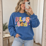Blessed DTF transfer with scrapbook-style polka-dot, plaid, and star paper cutout letters and a pink ribbon bow Shown on a Sapphire crewneck sweatshirt.